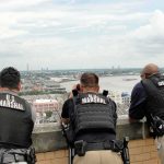 Three U.S. Marshals in tactical vests overlooking a city and river