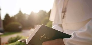 Person in white robe holding a Bible outdoors