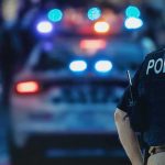 Bodycam Battle Ignites After Austin Shooting police officer in vest near patrol car with flashing lights