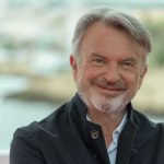 Sam Neill smiling in a dark jacket outdoors
