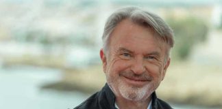 Sam Neill smiling in a dark jacket outdoors