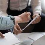 Jobs Whiplash: August Jumps, Trust Wobbles Hands of colleagues discussing a document during a meeting