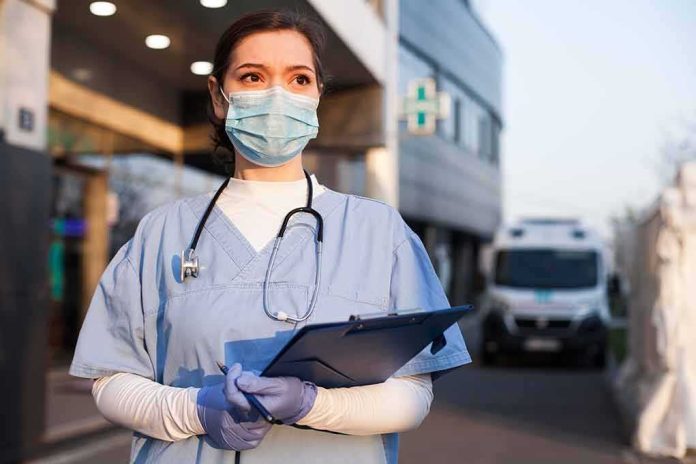 Healthcare worker in scrubs wearing mask and gloves holding a clipboard