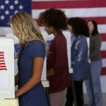 Voters at booths with American flags in a polling place