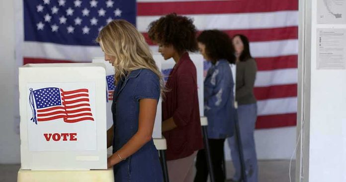 shutterstock_1740697532 Voters at booths with American flags in a polling place