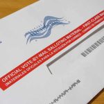 Mail-in ballot envelope with red label on wooden table