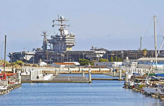 shutterstock_194774165-1 A large naval aircraft carrier docked in a harbor with smaller boats in the foreground