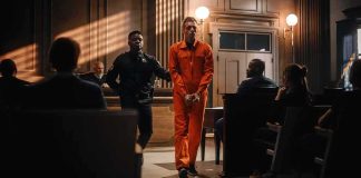 Inmate in orange jumpsuit escorted by officer in courtroom