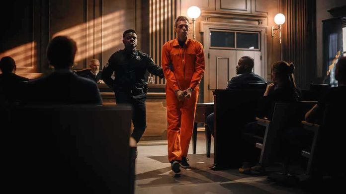 shutterstock_2056444856 Inmate in orange jumpsuit escorted by officer in courtroom