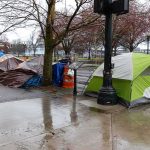 Tents lined along a wet city sidewalk on a rainy day