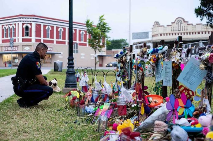 Police officer kneels at a memorial with flowers and crosses