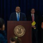 Man at podium during press conference with officials behind him