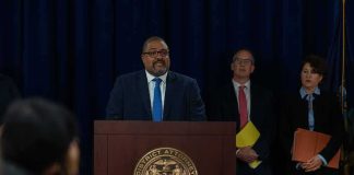 Man at podium during press conference with officials behind him
