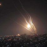 Night sky above a city with multiple rockets arcing and bright explosions