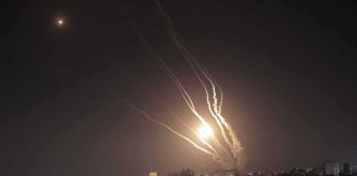 Night sky above a city with multiple rockets arcing and bright explosions