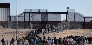 Crowd of people lining up near a border fence with barbed wire