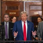 Donald Trump speaks at a courthouse hallway podium with officials standing behind him