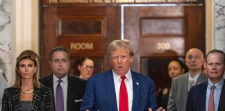 Donald Trump speaks at a courthouse hallway podium with officials standing behind him