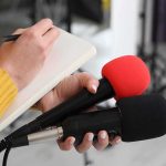 Presidential Jet Sparks Ethics Storm Journalist holding two microphones while writing in a notebook