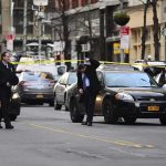 Police officers manage a taped-off city street with patrol cars and bystanders
