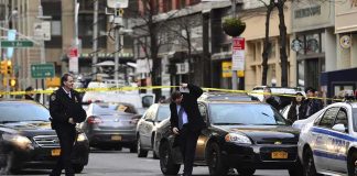 Police officers manage a taped-off city street with patrol cars and bystanders