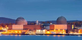 A Deeply Buried Nuclear Site Gets New Defenses nuclear power plant with two domed reactor buildings by water at dusk