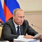 Vladimir Putin speaking at a meeting with documents and a microphone