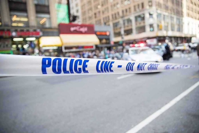 Police tape cordons off a city street with blurred buildings and patrol car