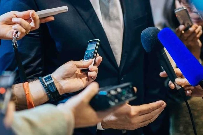 businessperson in suit surrounded by microphones and recorders