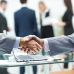 Businessmen handshake over a glass desk