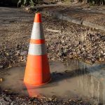 Highway 1 LOCKED—Tourism Cut Off Traffic cone in a water-filled pothole on a damaged road
