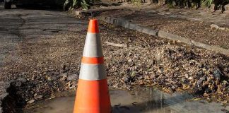 Traffic cone in a water-filled pothole on a damaged road