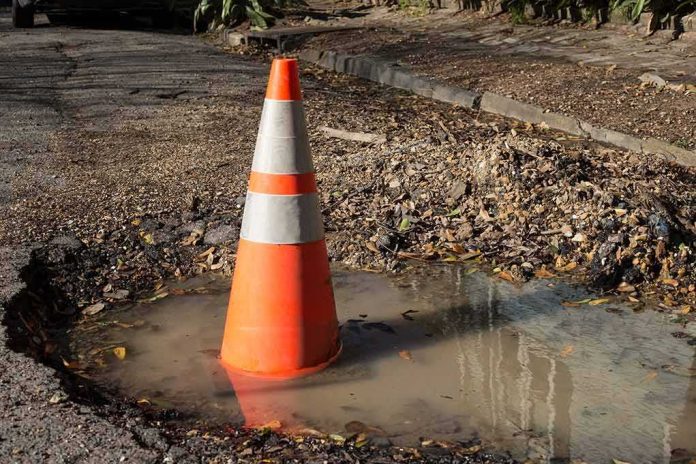 shutterstock_570874996 Traffic cone in a water-filled pothole on a damaged road