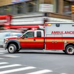 Robot Gatekeeps Emergencies in New Orleans Ambulance speeding through a city intersection with lights on
