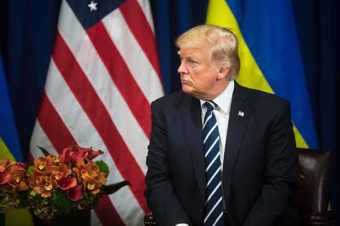 man in dark suit seated before US and Ukrainian flags