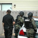 police officers in tactical gear beside patrol car