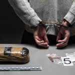 person in handcuffs behind back over table with seized packages