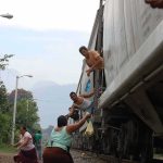 People on a moving freight train receive supplies from others on the ground