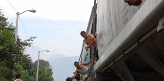 People on a moving freight train receive supplies from others on the ground