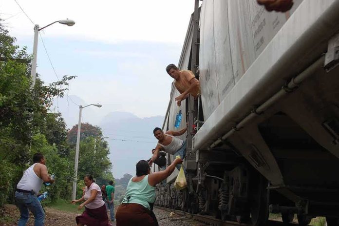 People on a moving freight train receive supplies from others on the ground