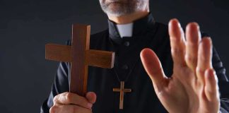 Clergyman holding wooden cross with hand raised