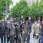group of masked protesters walking through a city street
