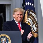 Donald Trump clapping at a podium with the presidential seal