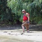 man in red life vest walking through muddy riverbank