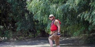 man in red life vest walking through muddy riverbank