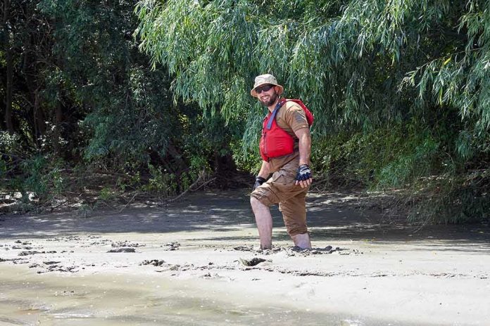 man in red life vest walking through muddy riverbank