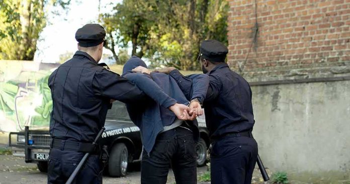 police officers arresting a person against a wall outdoors