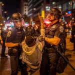 Police officers detain a protester at night on a city street